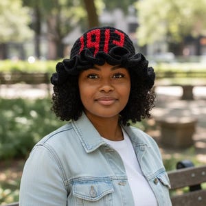 May include: Black crochet bucket hat with a ruffled brim. The hat features the red text "1919" on the crown. The person is wearing a light blue denim jacket and a white t-shirt.