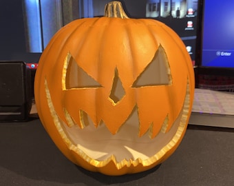 Puede incluir: Una calabaza naranja tallada con una cara de miedo. La calabaza tiene una amplia sonrisa con dientes y ojos brillantes.