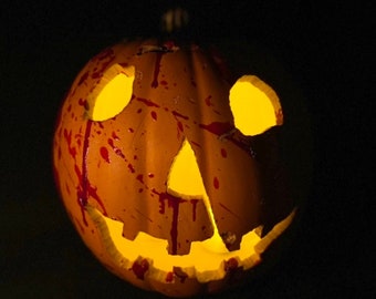 Może przedstawiać: Wyrzeźbiona pomarańczowa dynia z świecącym wnętrzem, przedstawiająca twarz jack-o'-lantern. Czerwone plamy przypominające krew znajdują się na powierzchni dyni, tworząc upiorną dekorację na Halloween.