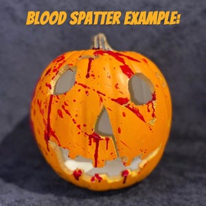 Puede incluir: Una calabaza naranja tallada con una cara de miedo, decorada con salpicaduras de sangre roja. El texto "BLOOD SPATTER EXAMPLE!" est&aacute; escrito encima de la calabaza.