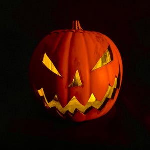 Puede incluir: Una calabaza naranja tallada con una vela encendida en su interior, creando una decoraci&oacute;n de Halloween espeluznante y festiva.