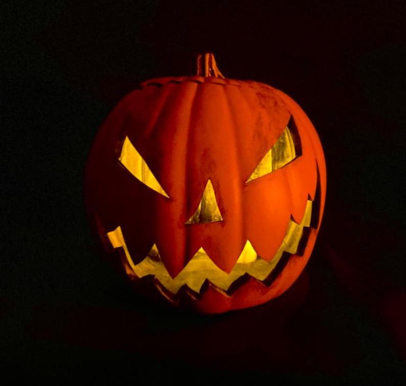 Puede incluir: Una calabaza naranja tallada con una vela encendida en su interior, creando una decoraci&oacute;n de Halloween espeluznante y festiva.