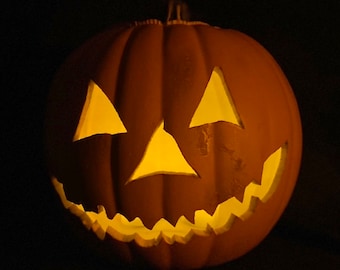 Puede incluir: Una calabaza tallada con una vela encendida en su interior. La calabaza tiene una cara tradicional de jack-o'-lantern con una amplia sonrisa, ojos triangulares y una boca dentada.