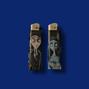 May include: Two black lighters with character illustrations. One lighter features a man in a suit, the other a woman in a blue dress and veil. Both lighters have silver metal tops and are set against a blue background.