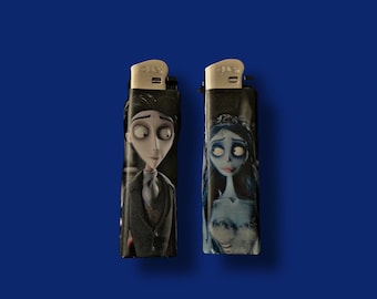May include: Two black lighters with character illustrations. One lighter features a man in a suit, the other a woman in a blue dress and veil. Both lighters have silver metal tops and are set against a blue background.