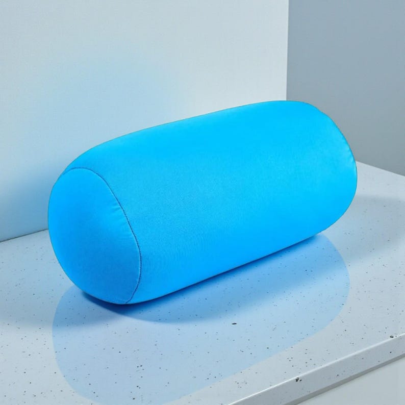 May include: A bright blue cylindrical pillow. The pillow is a solid color and has rounded ends. The pillow is made of a soft material and is designed for comfort and support. The pillow is a solid color and is placed on a light-colored surface.