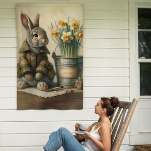 May include: A decorative wall hanging featuring a charming illustration of a rabbit wearing a plaid jacket. The artwork includes a galvanized bucket of daffodils and the word "SPRING". The overall color palette is soft and inviting.