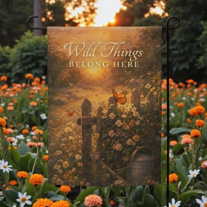 Op de afbeelding: Een tuinvaandel met een serene scène met vlinders, bloemen en een houten hek. De vlag toont de tekst "Wild Things Belong Here". Het kleurenpalet omvat warme tinten oranje, geel en bruin, wat een gevoel van rust oproept.