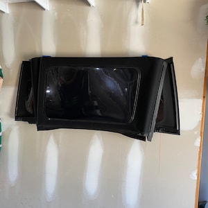 May include: Black Jeep Wrangler soft top with a rear window, folded and stored on a wall.