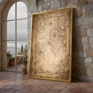 May include: A framed vintage nautical map with a gold frame. The map is tan and brown with a compass rose and other navigational details. The framed map is leaning against a stone wall next to a window.