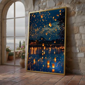 May include: A rectangular wall art piece in a gold frame depicting a night scene with numerous glowing orange paper lanterns floating in the dark blue sky and reflecting on the surface of a calm body of water, creating a warm, luminous contrast.
