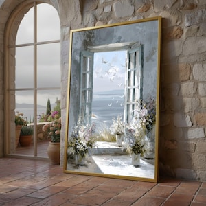 Puede incluir: Una pintura enmarcada representa una ventana abierta con una vista al mar y pájaros volando. La obra de arte tiene un marco dorado y está apoyada contra una pared de ladrillo. La escena incluye flores blancas en macetas y una vista del océano.