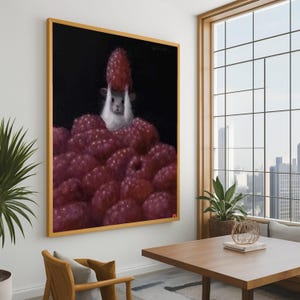 May include: A framed painting depicts a white and gray rodent holding a large red raspberry above a pile of other raspberries. The background is black, and the painting is in a gold frame. The artwork is displayed in a room with a large window.