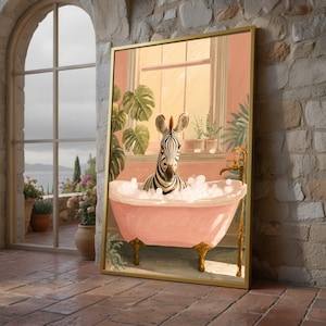 May include: A framed art print shows a zebra in a pink clawfoot bathtub with bubbles. The zebra's head and ears are visible above the bubbles. The background features a window, plants, and a peach wall. The frame is gold-coloured.