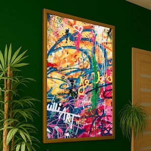 May include: A framed abstract art piece with a vibrant mix of colors. The artwork features splatters and streaks of blue, yellow, orange, pink, and white paint, with the word "ART" visible. The frame is a warm brown color.