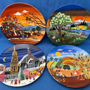 May include: Four decorative ceramic plates with colorful, hand-painted scenes depicting seasonal landscapes. Each plate features a unique design, including autumn vineyards, spring blossoms, a winter town, and a summer harvest.