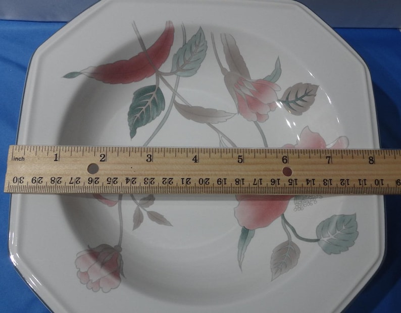 May include: White octagonal ceramic dinner plate with a floral design featuring pink and red flowers, green leaves, and a brown stem. The plate measures approximately 8 inches in diameter.
