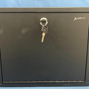 May include: Black metal lockable cabinet with a key in the lock. The cabinet has a silver ADIRoffice logo on the front.