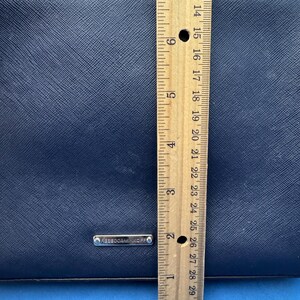 Puede incluir: Un bolso de mano azul marino con cremallera plateada y correa de cadena. El bolso mide aproximadamente 18 cm de alto. La marca "REBECCAMINKOFF" es visible en una peque&ntilde;a placa plateada.