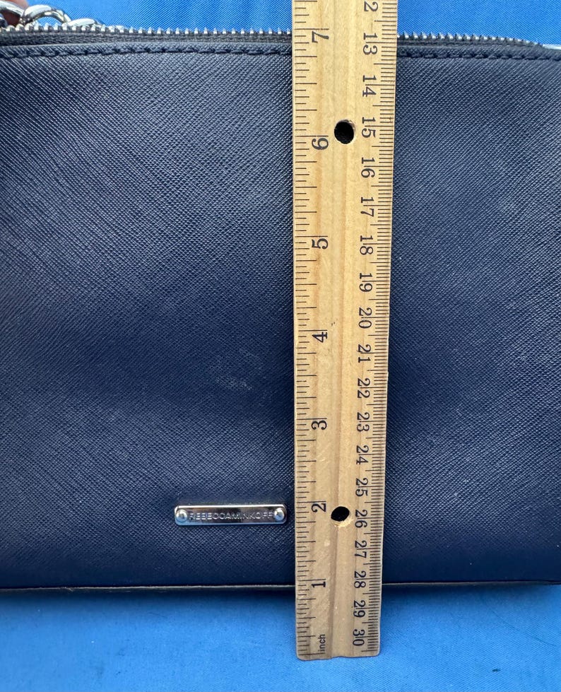 Puede incluir: Un bolso de mano azul marino con cremallera plateada y correa de cadena. El bolso mide aproximadamente 18 cm de alto. La marca "REBECCAMINKOFF" es visible en una peque&ntilde;a placa plateada.