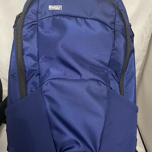 May include: A navy blue backpack with black zippers and accents. The backpack has a padded back and shoulder straps. The brand name "MindShift" is visible on the front. The backpack is designed for outdoor activities.