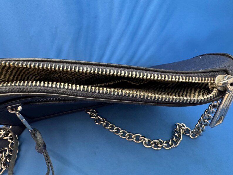 Puede incluir: Un bolso bandolera azul marino con una cadena plateada. El bolso tiene un cierre de cremallera y un forro interior estampado. La cremallera es plateada y el bolso est&aacute; hecho de un material liso.
