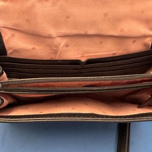 Może przedstawiać: Czarna sk&oacute;rzana torba crossbody, otwarta, aby odsłonić wiele przegr&oacute;dek na karty i przegrodę zapinaną na zamek. Wnętrze jest w kolorze jasnor&oacute;żowym z wzorem w kropki. Torba ma złoty zamek błyskawiczny i okucia.