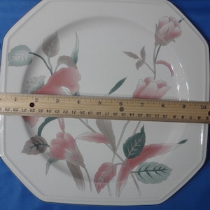 May include: White octagonal ceramic dinner plate with a floral design featuring pink and green flowers. The plate has a slightly raised rim.