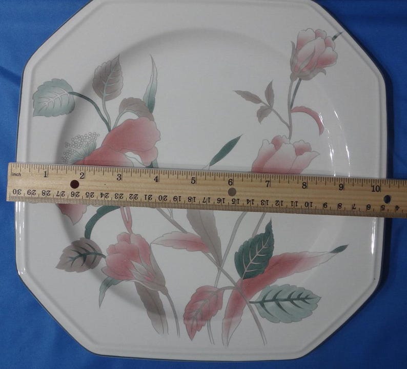 May include: White octagonal ceramic dinner plate with a floral design featuring pink and green flowers. The plate has a slightly raised rim.