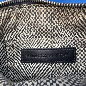 Puede incluir: Primer plano del interior de un bolso negro. El forro presenta un patr&oacute;n geom&eacute;trico en blanco y negro. Se ve una etiqueta de cuero negro con el texto en relieve "REBECCAMINKOFF".