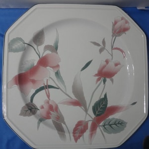 May include: A white octagonal ceramic dinner plate with a floral design. The plate features pink and green flowers with leaves on a white background.