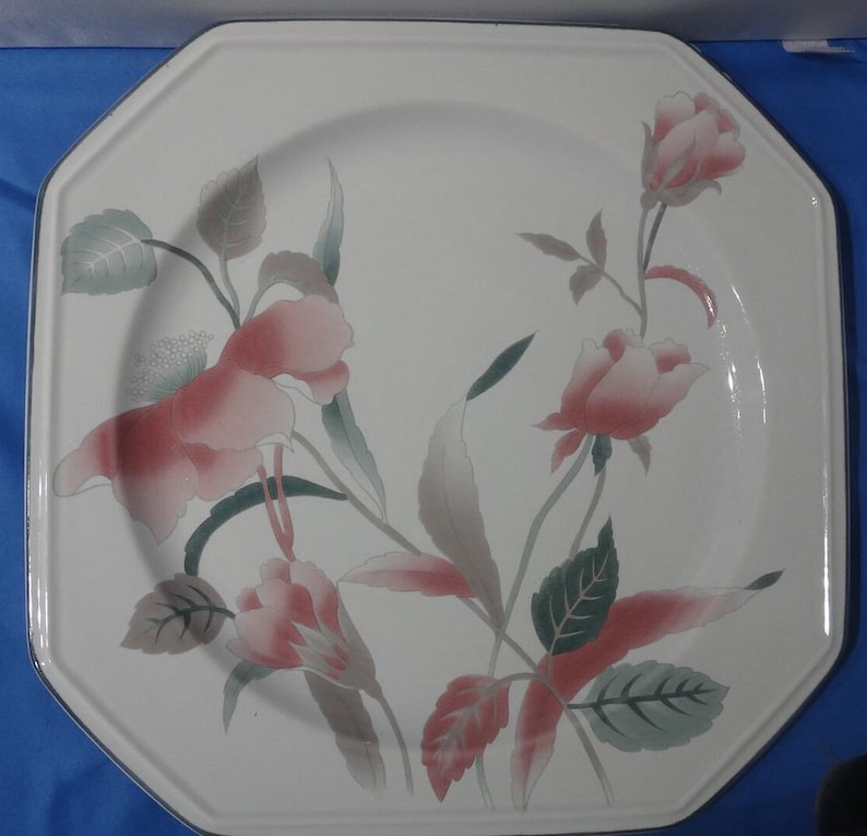 May include: A white octagonal ceramic dinner plate with a floral design. The plate features pink and green flowers with leaves on a white background.