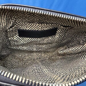 Puede incluir: Vista interior de una bolsa negra con cremallera y forro estampado en blanco y negro. El forro presenta una mezcla de patrones de chevron y cuadrados peque&ntilde;os. Una etiqueta negra est&aacute; cosida en el interior de la bolsa.