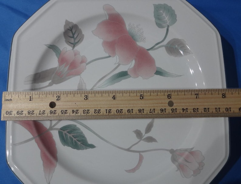 May include: Octagonal white ceramic dinner plate with a floral design featuring pink and green flowers. The plate measures 8 inches in diameter.
