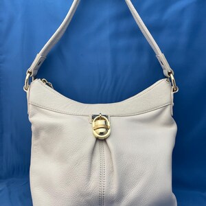 May include: A light gray leather shoulder bag with a single strap. The bag has a gold-colored clasp and zipper. The bag is made of soft leather and has a simple, elegant design.