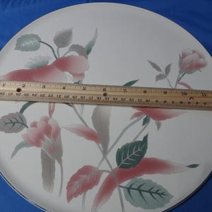 May include: A white ceramic dinner plate with a floral design featuring pink and green flowers. The plate has a black rim.