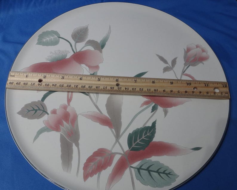 May include: A white ceramic dinner plate with a floral design featuring pink and green flowers. The plate has a black rim.