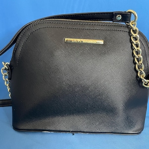 May include: Black crossbody bag with a gold chain strap and a gold metal logo that reads "Steve Madden".