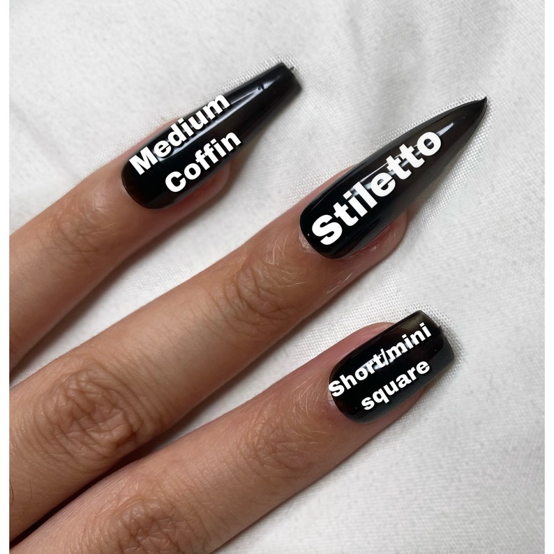 May include: A hand model wearing black press-on nails in four different shapes: medium coffin, stiletto, short/mini square.