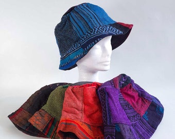 May include: A collection of patchwork bucket hats in various colors, including blue, red, green, and purple. The hats feature a mix of patterned and solid fabric panels. One hat is displayed on a white mannequin head.