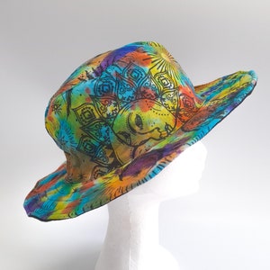 May include: A colorful sun hat with a tie-dye pattern and a black mandala design. The hat features a sun with a face and a floral design.