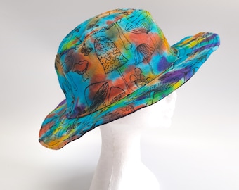 May include: A colorful tie-dye bucket hat with a black mushroom pattern. The hat features a vibrant mix of blue, orange, yellow, and purple hues. The brim is wide, and the hat is displayed on a white mannequin head.