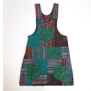 May include: A patchwork overall dress featuring a combination of brown, green, blue and red fabrics. The dress has a square neckline and two pockets on the front.