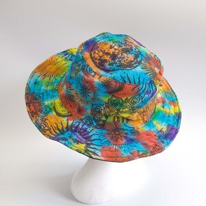 May include: A blue, orange, yellow, and purple tie-dye bucket hat with a black and white mandala design featuring a sun, moon, and stars.