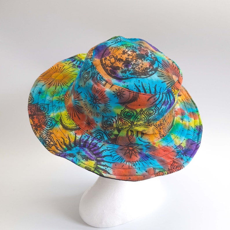 May include: A blue, orange, yellow, and purple tie-dye bucket hat with a black and white mandala design featuring a sun, moon, and stars.