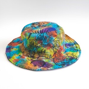 May include: A colorful bucket hat with a tie-dye pattern and a black mandala design featuring a sun and moon. The hat is made of cotton and has a wide brim.