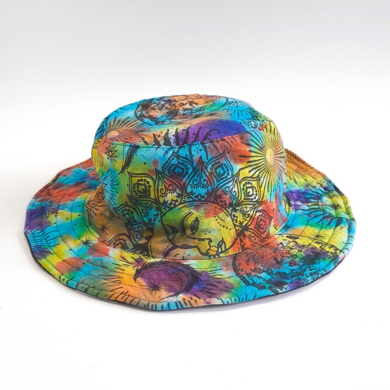 May include: A colorful bucket hat with a tie-dye pattern and a black mandala design featuring a sun and moon. The hat is made of cotton and has a wide brim.