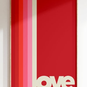 Puede incluir: Una impresi&oacute;n enmarcada con un fondo rojo y rayas verticales en tonos de rojo, rosa y crema. La palabra "love" est&aacute; impresa en blanco en la parte inferior de la impresi&oacute;n.