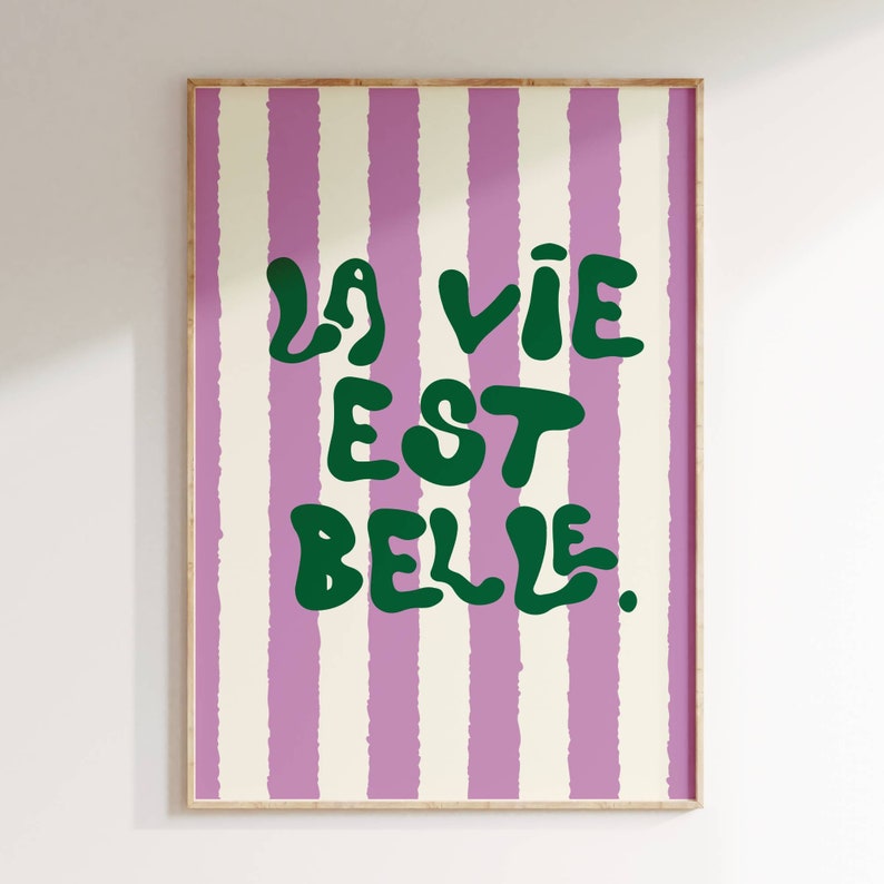 May include: A framed print with a pink and white striped background. The text "La vie est belle." is written in green, bubbly letters.
