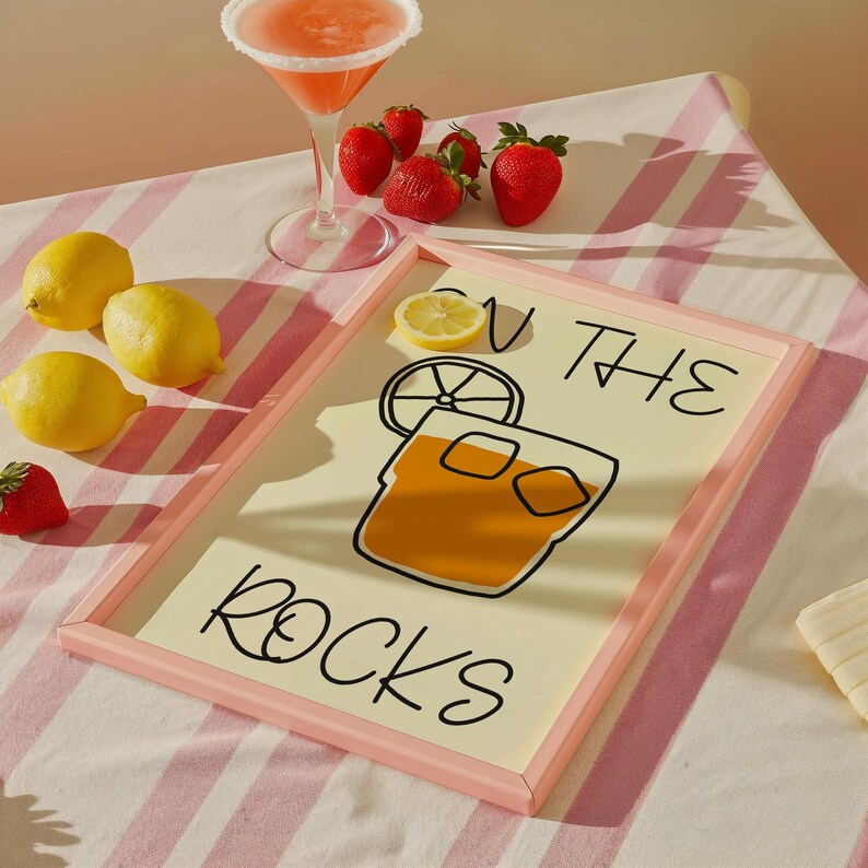 May include: A pink framed print with the text "On the Rocks" and a cartoon illustration of a glass of ice with a lemon wedge.
